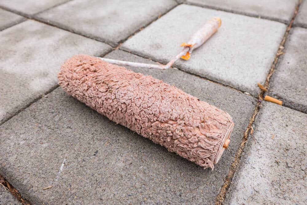 Rouleau appliquant un primaire d'accrochage de couleur rose sur un sol gris en ragréage autolissant.