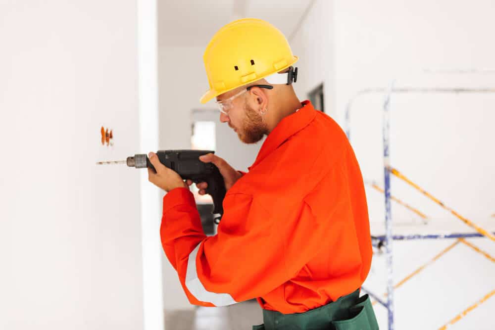 Personne utilisant un perforateur pour percer un trou dans un mur porteur en béton afin d'y fixer une cheville.