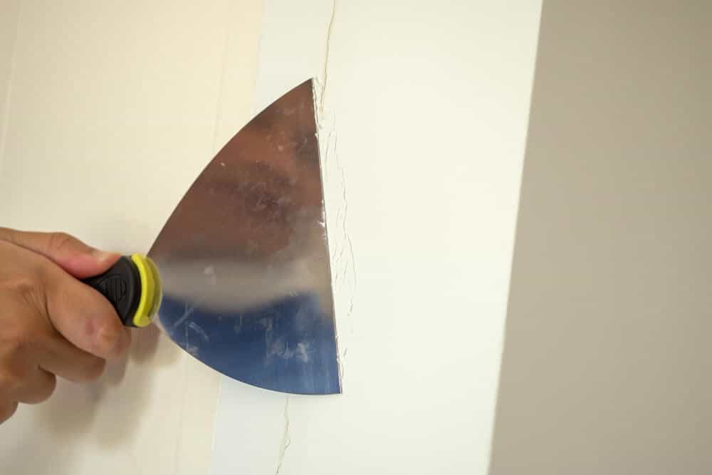 Spatule appliquant de l'enduit de rebouchage sur une fissure dans un mur en briques plâtrières recouvert de plâtre.