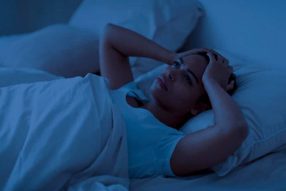 Personne éveillée dans son lit la nuit, écoutant attentivement un bruit avec une expression inquiète.